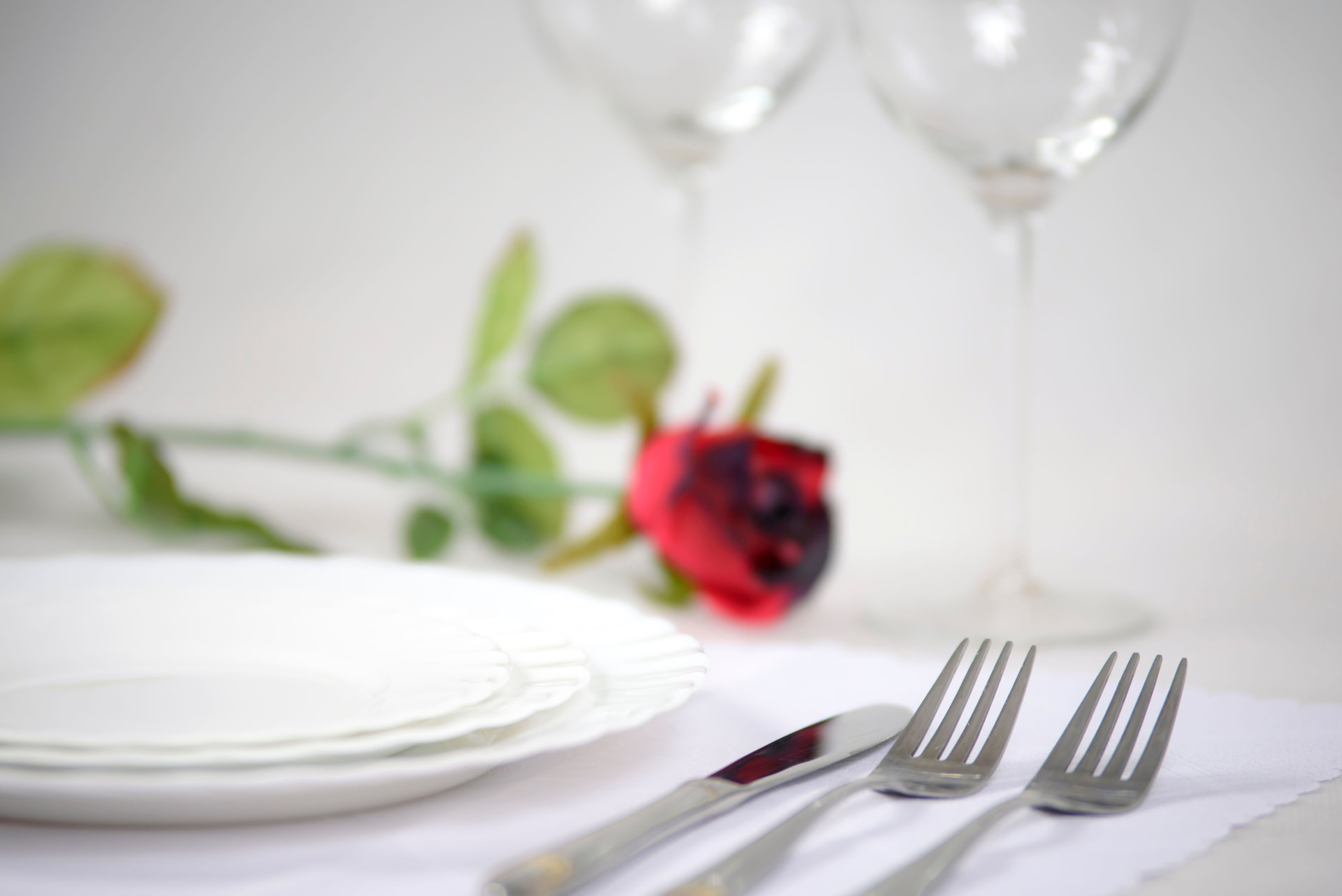 Table de mariage dressée avec des assiettes blanches et une rose rouge